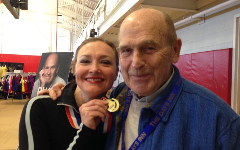Allison holding a gold medal next to Dick Button, for the manleywoman skatecast, a figure skating podcast